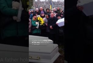 A father gently rocks the small coffin of his one-year-old son.